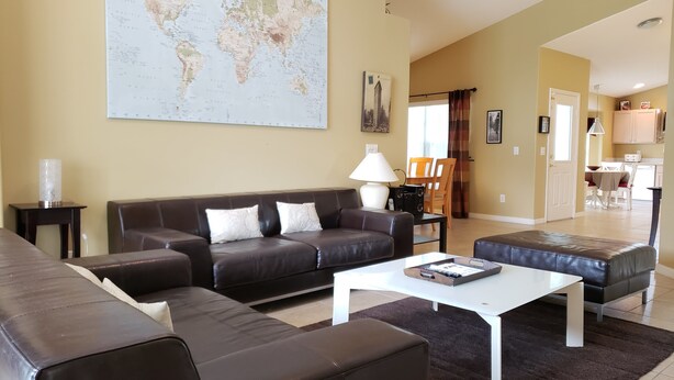 Ein Wohnzimmer mit einer großen Weltkarte, einem braunen Ledersofa, einem weißen Couchtisch und einem Essbereich im Hintergrund.