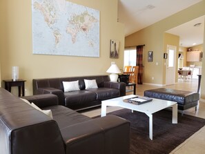 Een woonkamer met een grote wereldkaart, een bruine leren bank, een witte salontafel en een eethoek op de achtergrond.