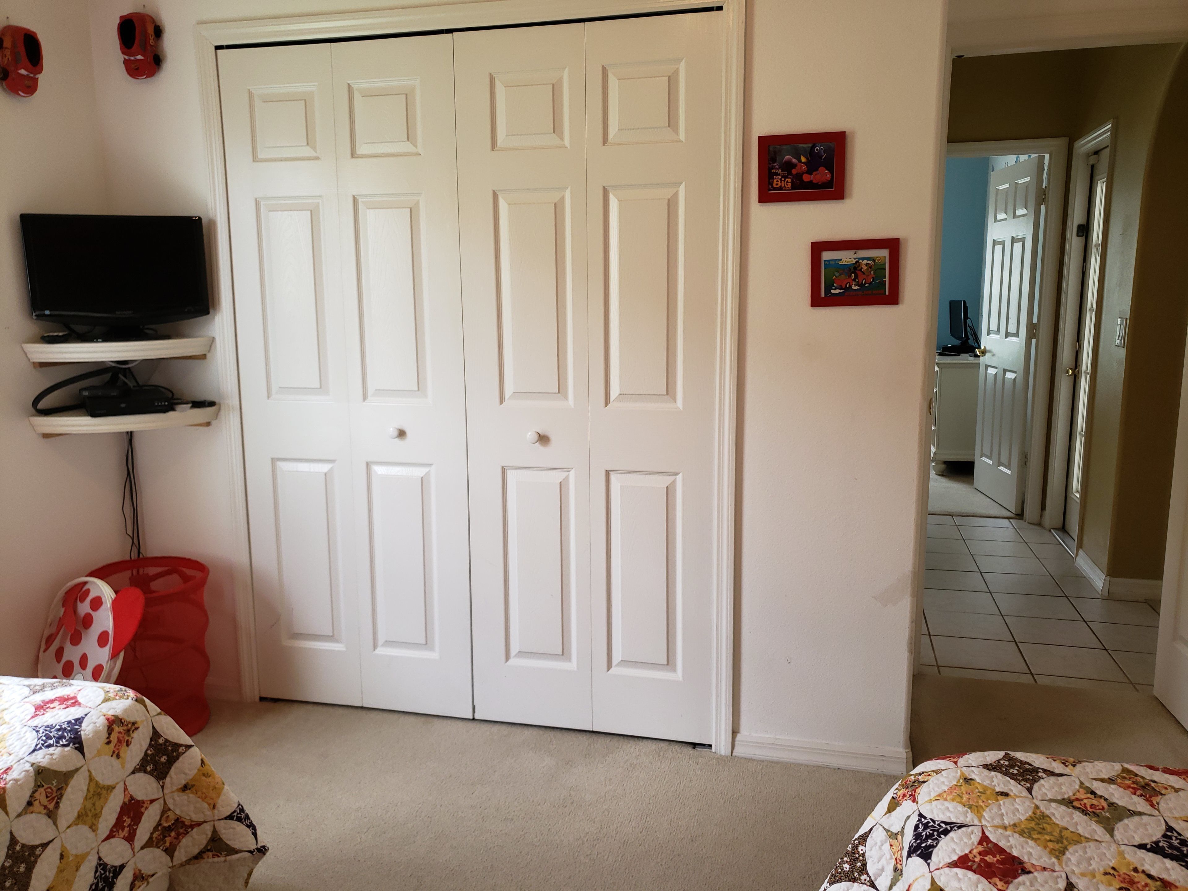 A bedroom with a white door, a television on a shelf, and a red bag.