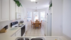 A modern kitchen with white cabinets, a stove, and a dining area with a table and chairs. - Windsor Hills 7788 (Kissimmee)
