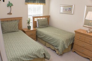 A bedroom with two single beds, a nightstand, a dresser, a potted plant, and a window with blinds. - Coral Cay 2412 (Kissimmee)