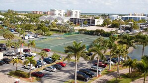 Un parking avec plusieurs voitures, un court de tennis et des palmiers.