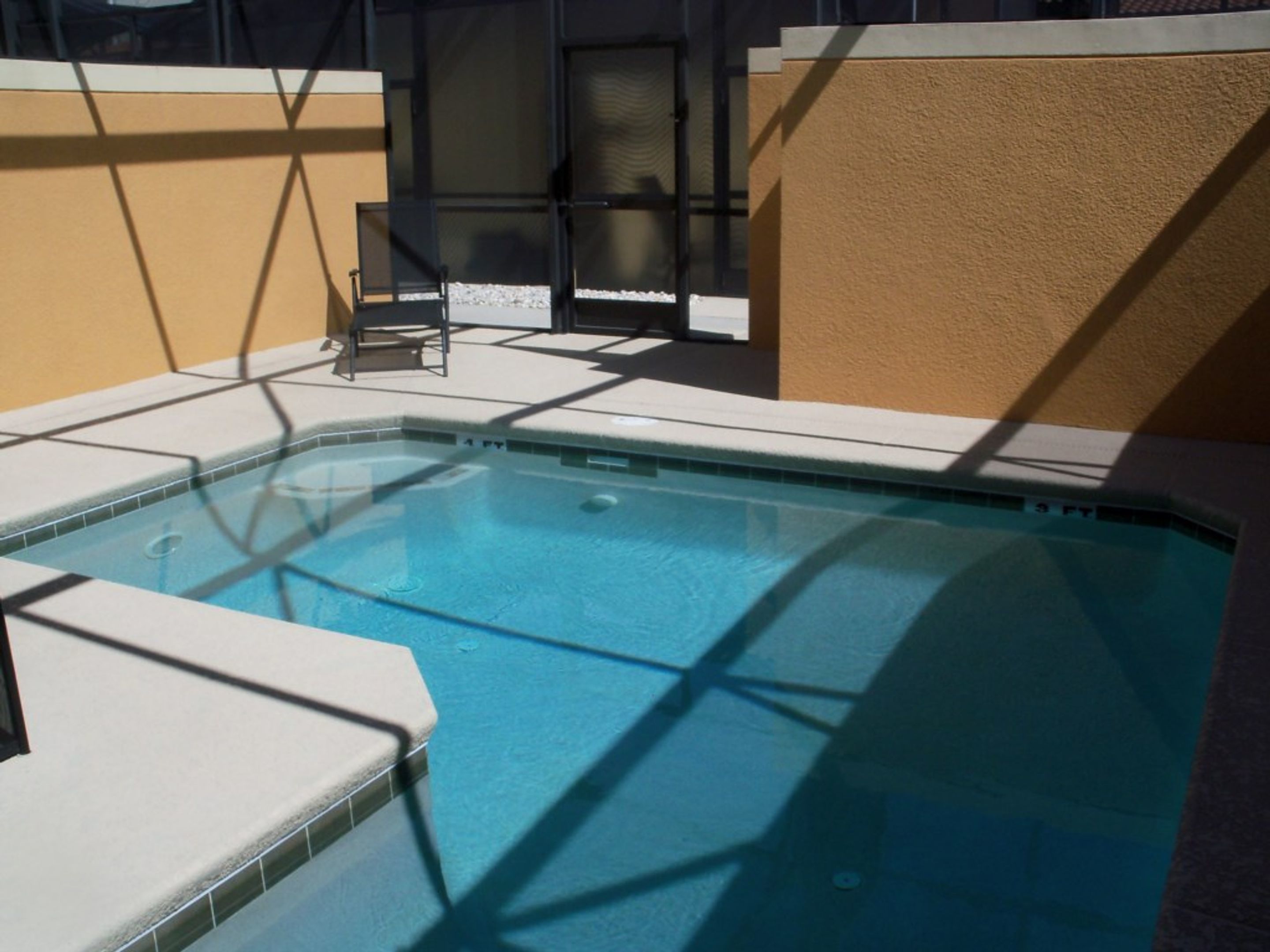 A swimming pool with a tiled edge, a chair, and a sunshade.