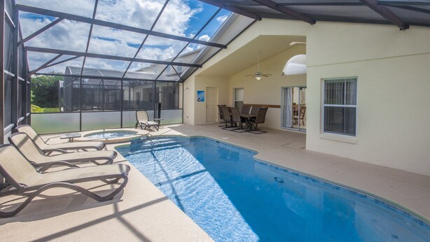 Une piscine couverte avec des chaises longues, un jacuzzi et un coin repas équipé d’un ventilateur de plafond.