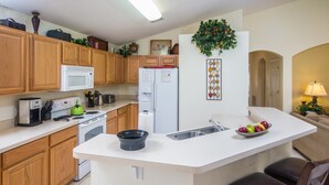 Une cuisine avec des meubles de rangement en bois, un plan de travail blanc, un four à micro-ondes, une cuisinière, un réfrigérateur et un évier.