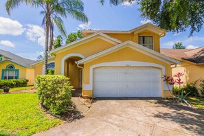 A two-story house with a yellow facade, a white garage door, and a well-maintained lawn. - Lindfields 3002 (Kissimmee)