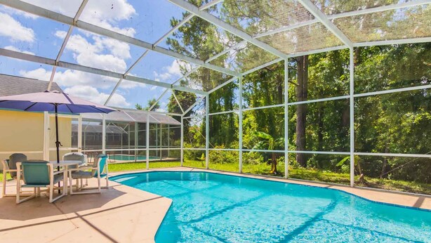 A covered swimming pool with a glass enclosure, surrounded by greenery. - Lindfields 3002 (Kissimmee)