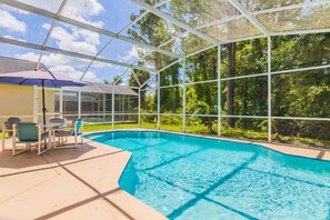 A covered swimming pool with a glass enclosure, surrounded by greenery. - Lindfields 3002 (Kissimmee)