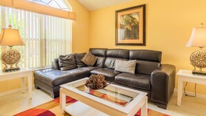 A living room with a leather sofa, a glass coffee table, and a framed picture on the wall. - Lindfields 3002 (Kissimmee)