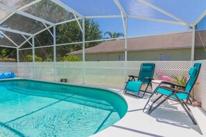 A swimming pool with a covered area, lounge chairs, and a house in the background.