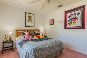 A bedroom with a bed, Mickey and Minnie Mouse decor, framed pictures, and a nightstand with lamps.