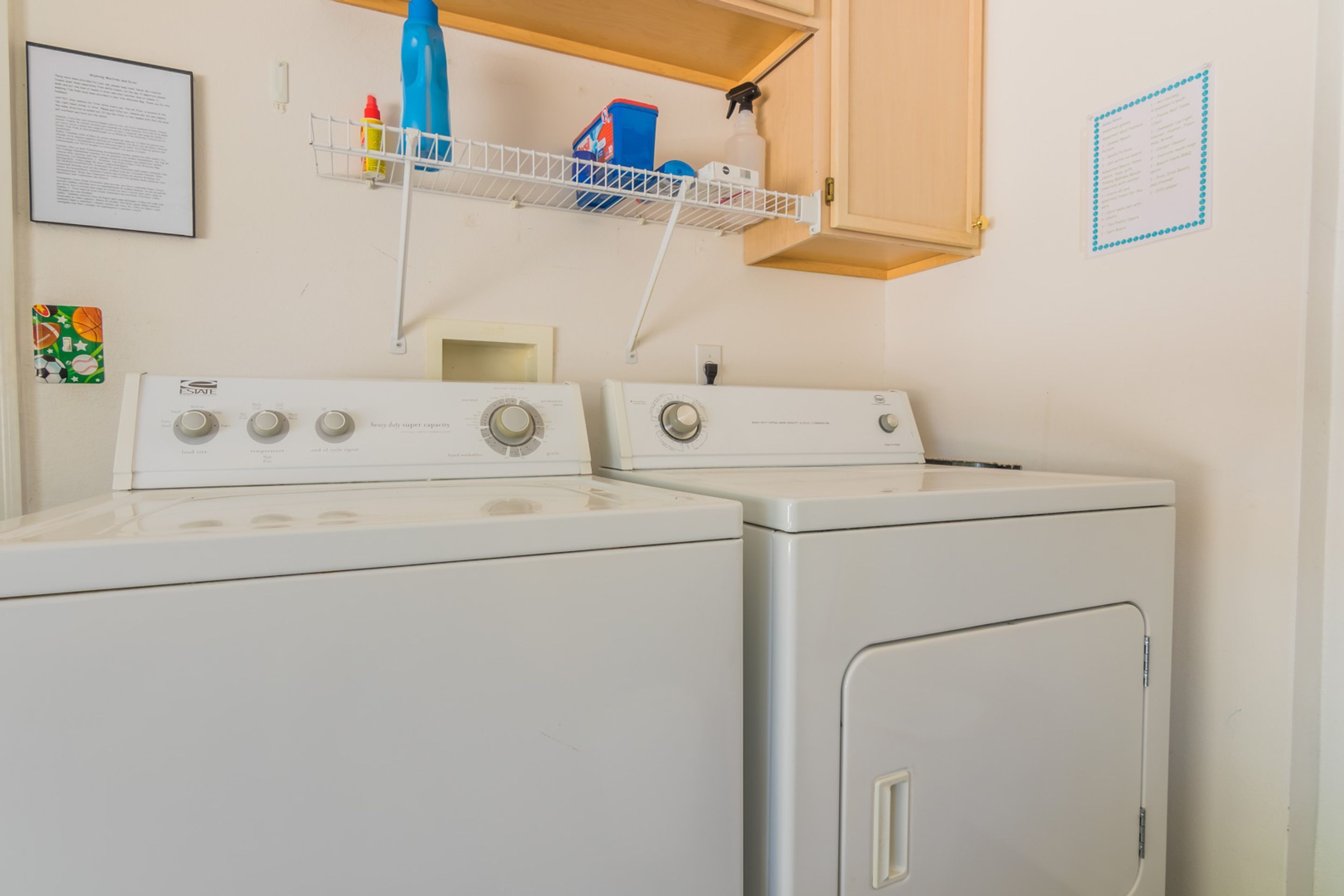 A laundry area with two front-loading washing machines, a shelf above holding cleaning supplies, and a cabinet with a wooden door.