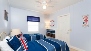 A bedroom with two beds, a ceiling fan, a window with blinds, a door, and a wall decoration. - Fort Myers Beach Area 2670 (Fort Myers Beach)