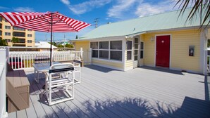 A wooden deck with a red and white striped umbrella, a white chair, and a yellow building with a red door. - Fort Myers Beach Area 2670 (Fort Myers Beach)