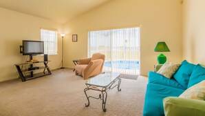 A living room with a glass coffee table, beige armchair, teal sofa, and a television on a stand. - The Palms at Lake Davenport 647 (Davenport)
