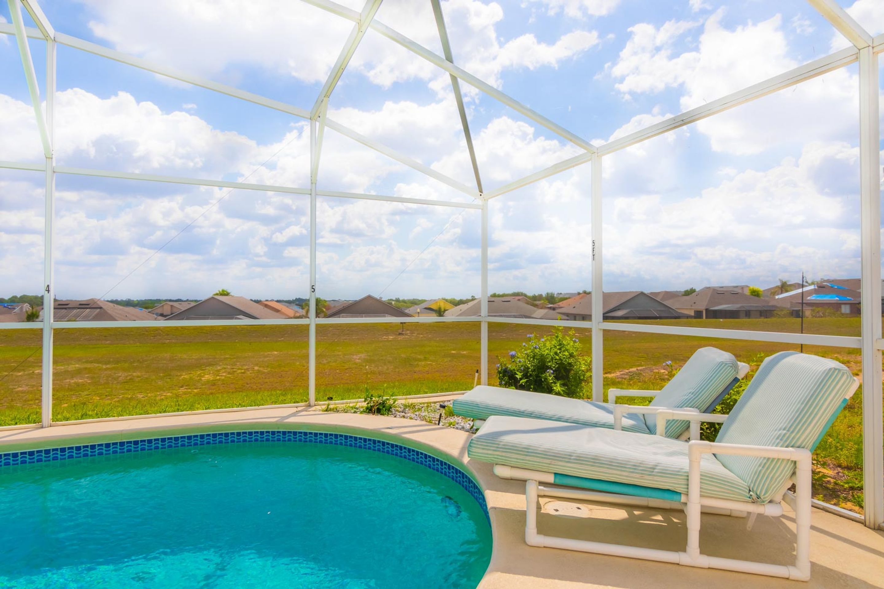 A covered swimming pool with lounge chairs and a view of a residential area.