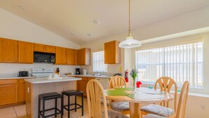 A modern kitchen with wooden cabinets, a central island with stools, and a dining table with chairs. - The Palms at Lake Davenport 647 (Davenport)