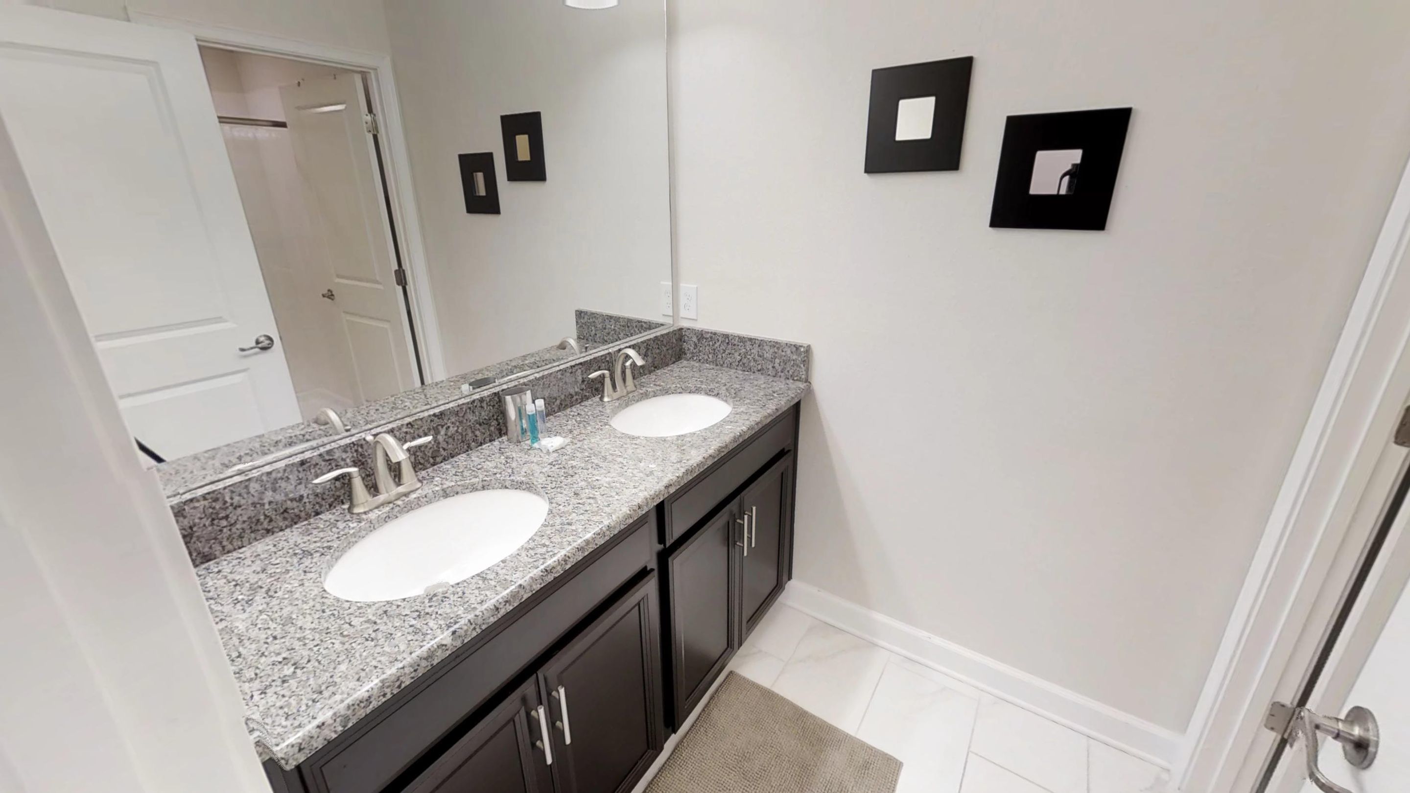 A bathroom with two sinks, dark cabinets, a large mirror, and a door.