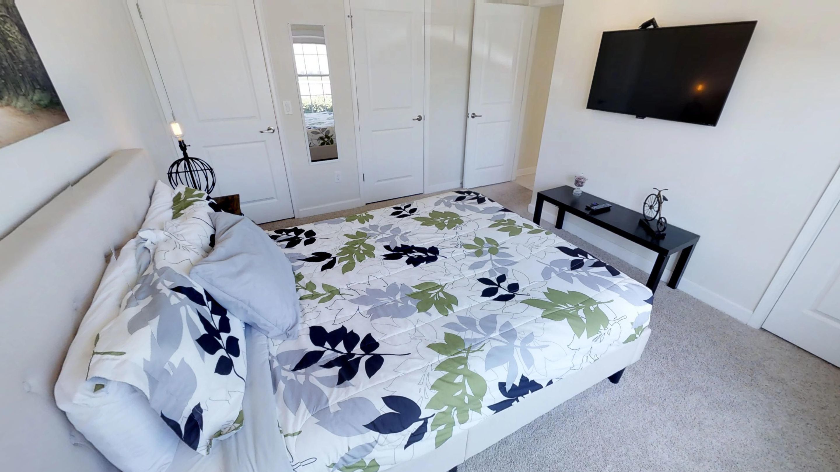 A bedroom with a bed, a TV mounted on the wall, and a small table with a bicycle.
