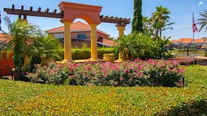 Un jardín con una pérgola, palmeras y un edificio de techo rojo.