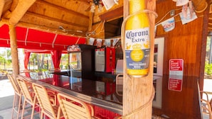 Una zona de bar con una botella de cerveza Corona Extra, sillas rojas y techo de madera.
