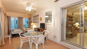 A room with a round table, white chairs, a ceiling fan, a television, and a sliding glass door leading to another room. - Bonita Springs 92 (Bonita Springs)