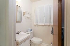 Ein kleines, sauberes Badezimmer mit Toilette, Waschbecken und Spiegel. An der Wand befinden sich zwei Handtuchhalter und eine Duschvorhang.