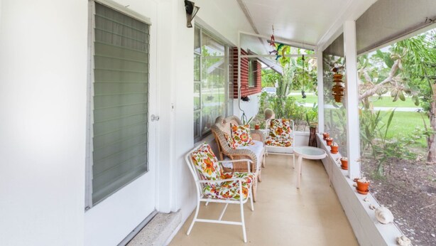 A covered porch with white wicker chairs and a small table, surrounded by potted plants. - Bonita Springs 92 (Bonita Springs)