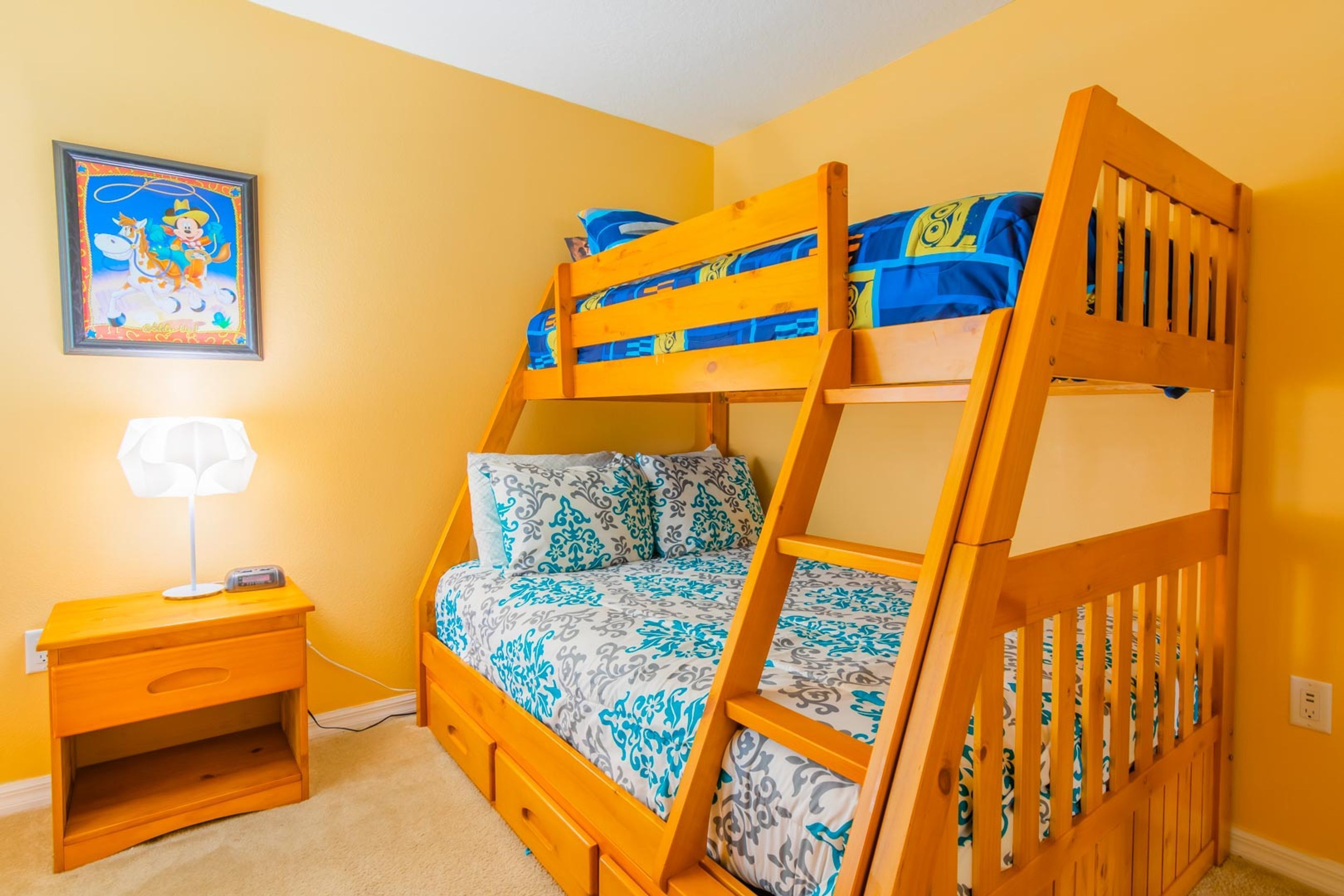 A bunk bed room with a nightstand, a lamp, and a framed picture on the wall.