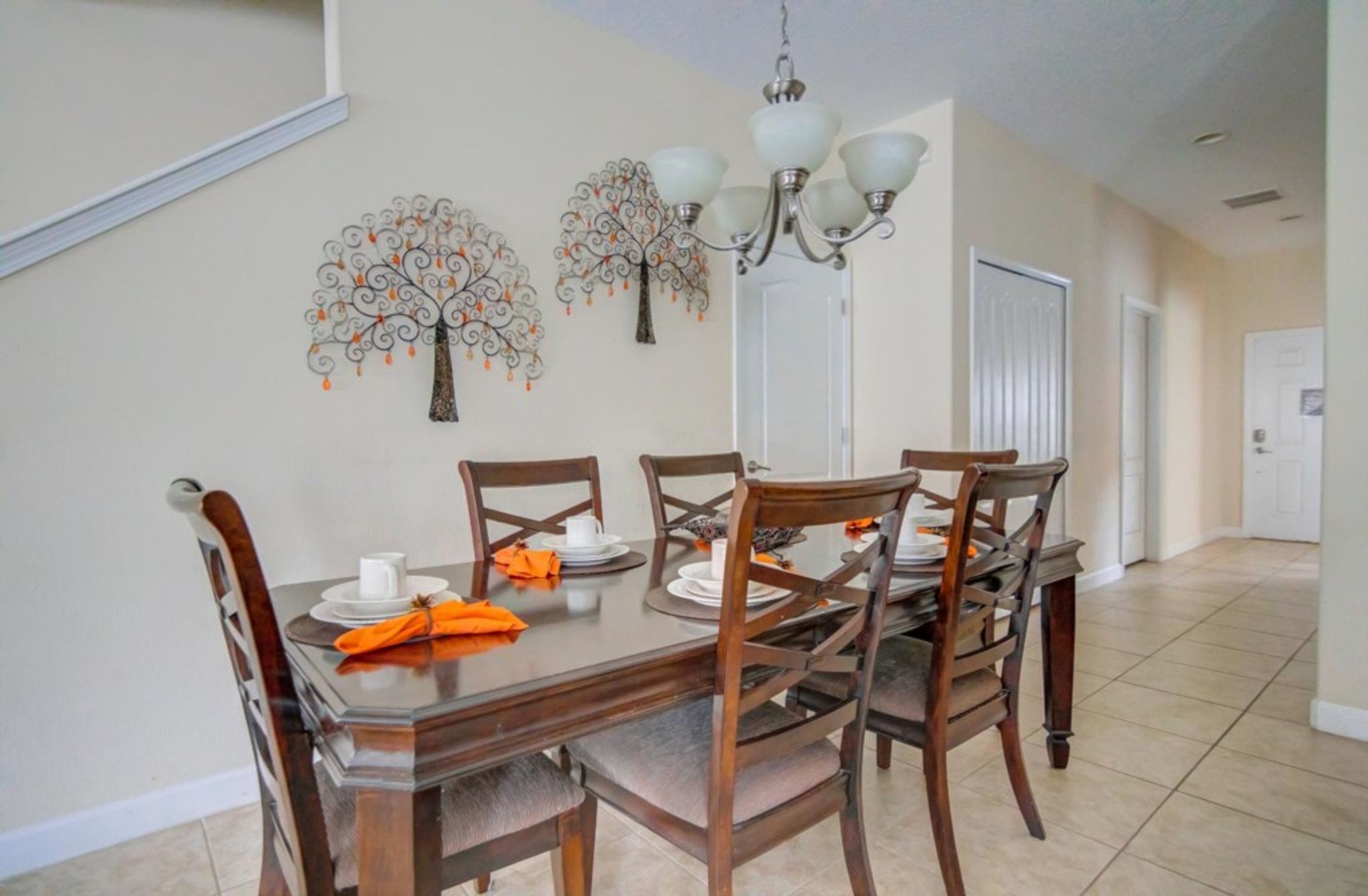 Un coin repas avec une table en bois dressée pour quatre personnes, entourée de chaises. Des œuvres d’art décoratives ornent le mur au-dessus de la table, et un lustre est suspendu au plafond.