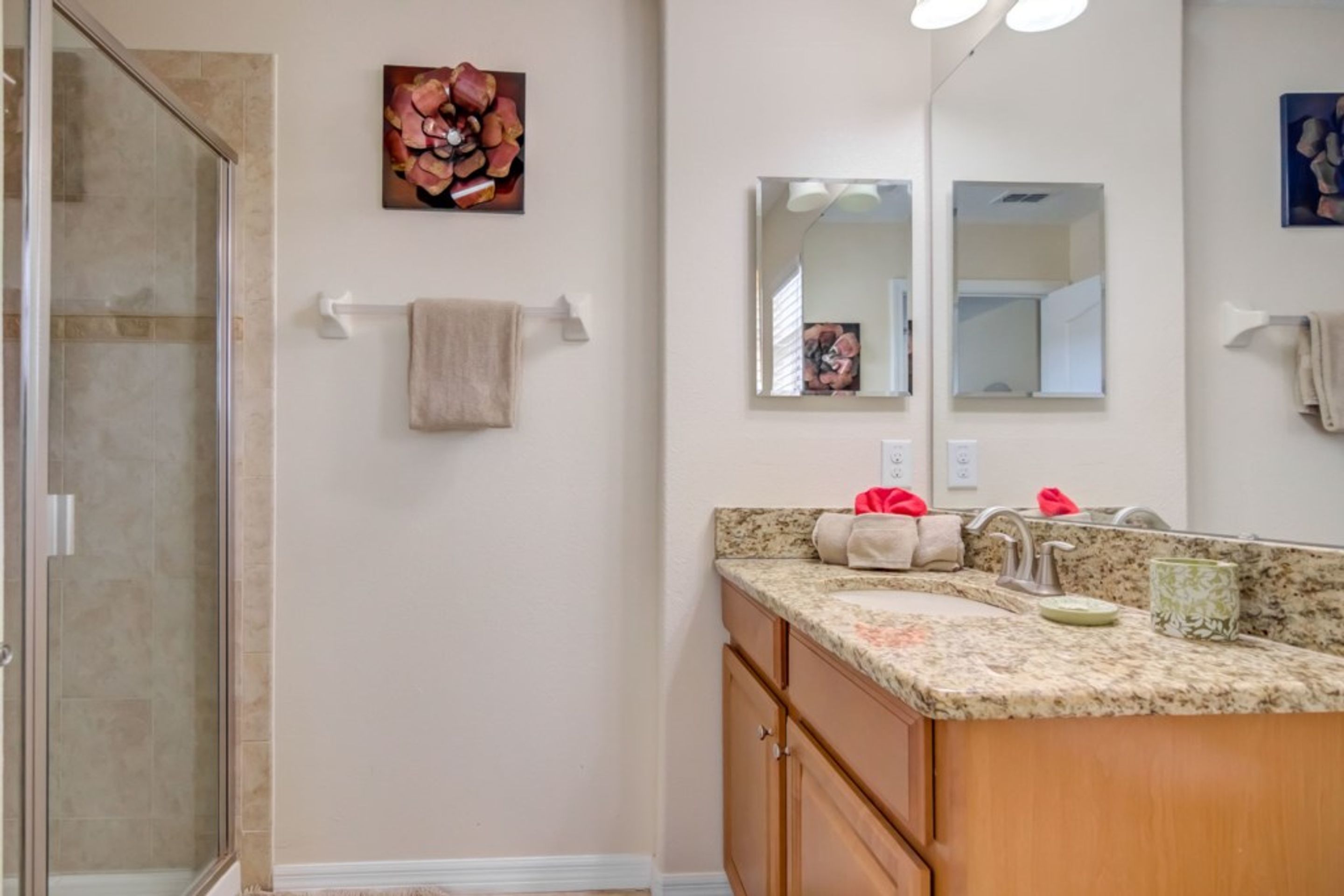 A bathroom with a glass shower enclosure, a granite countertop sink, and wooden cabinets.