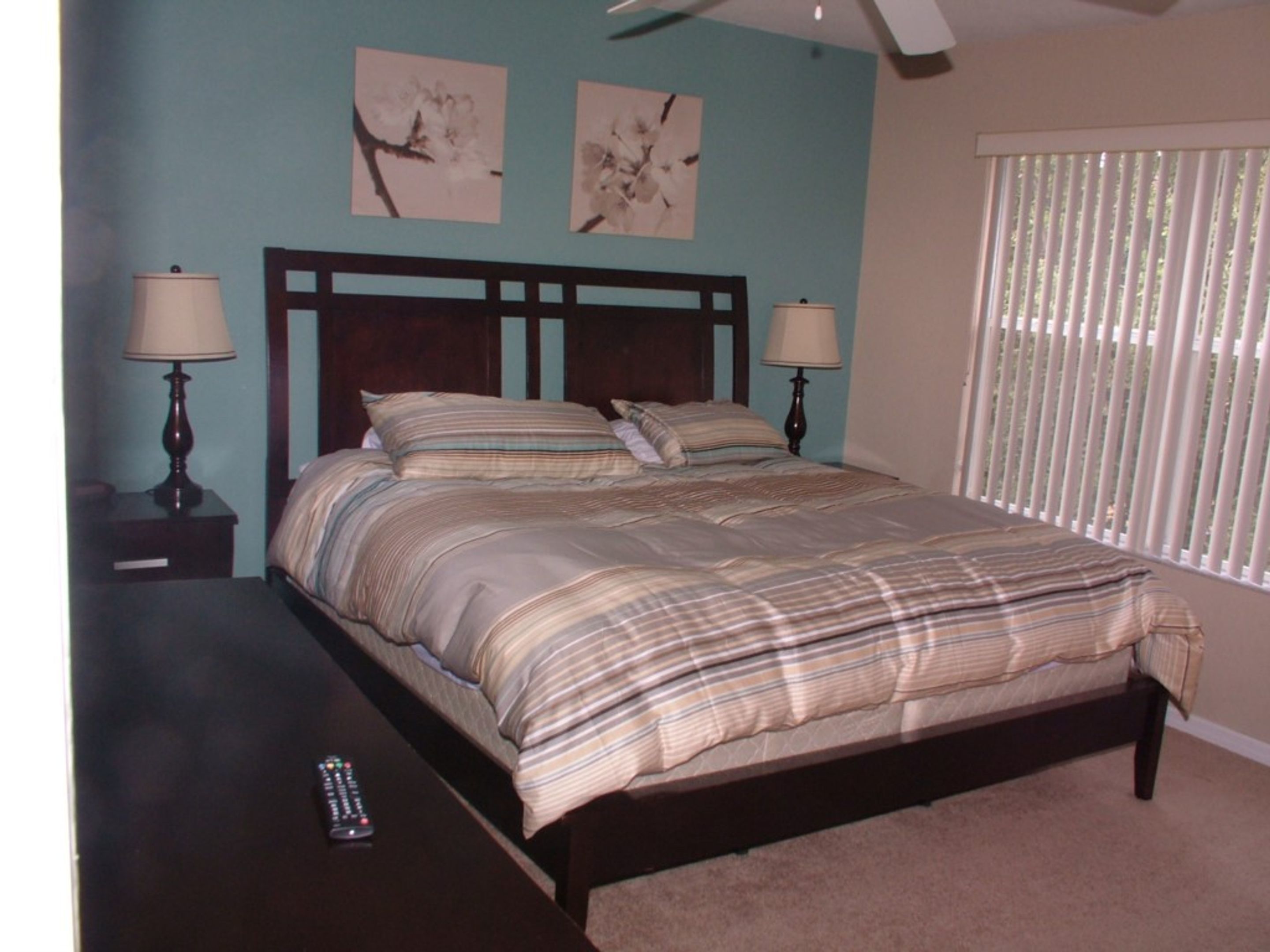 A bedroom with a bed, two bedside tables with lamps, a window with blinds, and two wall art pieces.