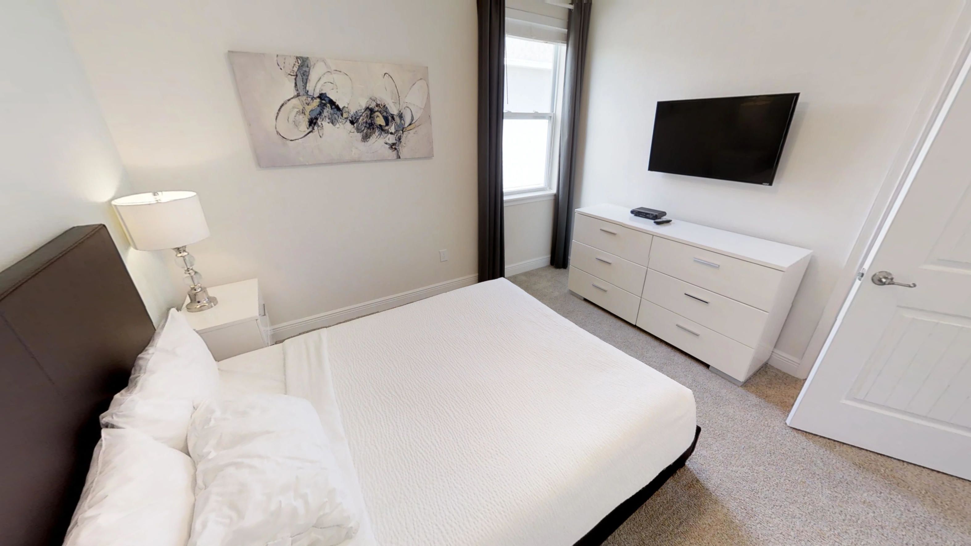 Een slaapkamer met een bed, een dressoir, een televisie en een schilderij aan de muur.