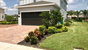 A two-story house with a garage, a well-maintained lawn, and a brick driveway. - Encore Resort at Reunion 7705 (Kissimmee)