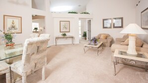 A spacious living room with a glass coffee table, beige sofas, and a patterned armchair. - Highlands Reserve Golf & Country Club 1114 (Davenport)