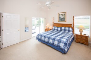 A bedroom with a bed, a ceiling fan, a nightstand with a lamp, a window with blinds, and a door. - Highlands Reserve Golf & Country Club 1114 (Davenport)