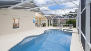 A swimming pool with a glass enclosure, a covered patio area with chairs, and a view of the surrounding landscape. - Highlands Reserve Golf & Country Club 1114 (Davenport)