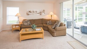 A living room with a sectional sofa, two side tables, a coffee table, and a large window with blinds. - Highlands Reserve Golf & Country Club 1114 (Davenport)