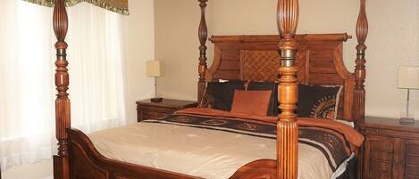 A four-poster bed with a wooden headboard and footboard, a ceiling fan, and a nightstand with a lamp.