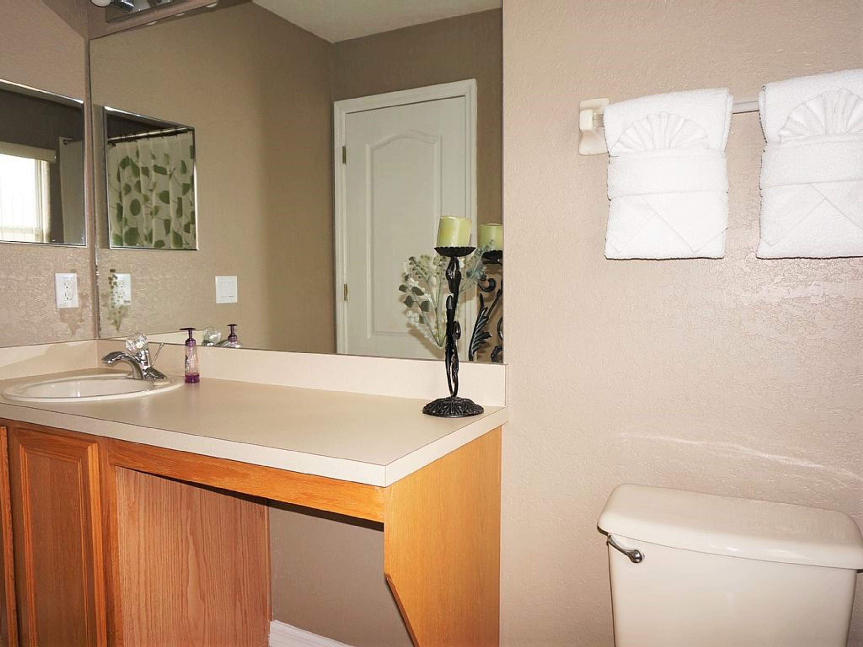 A bathroom with a sink, mirror, toilet, and towels on the wall.