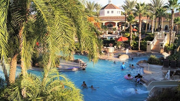 A pool area with palm trees, a boat, and a building in the background. - Regal Palms Resort & Spa 1215 (Davenport)