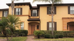 A two-story building with a yellow facade, brown shutters, and a brick pathway leading to the entrance. - Regal Palms Resort & Spa 1215 (Davenport)