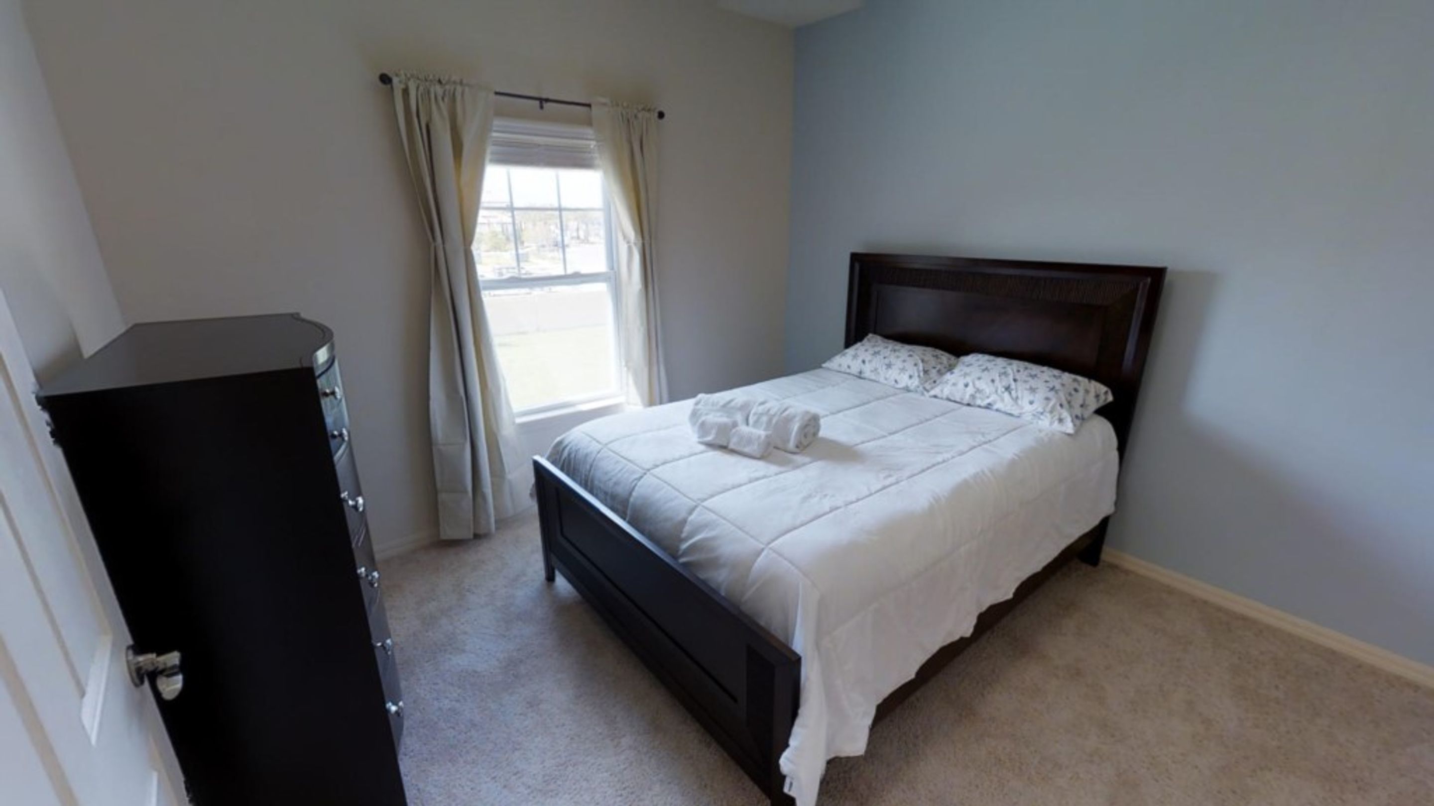 Un dormitorio con cama, cómoda y ventana con cortinas.