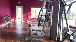 A gym with various exercise equipment, a red wall, and large windows. - West Lucaya 8996 (Kissimmee)