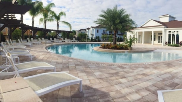 A pool area with lounge chairs and a building with large windows. - West Lucaya 8996 (Kissimmee)