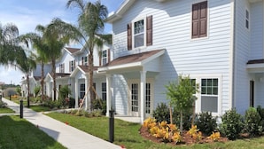 A row of white two-story houses with brown shutters, a sidewalk, and small trees. - West Lucaya 8996 (Kissimmee)
