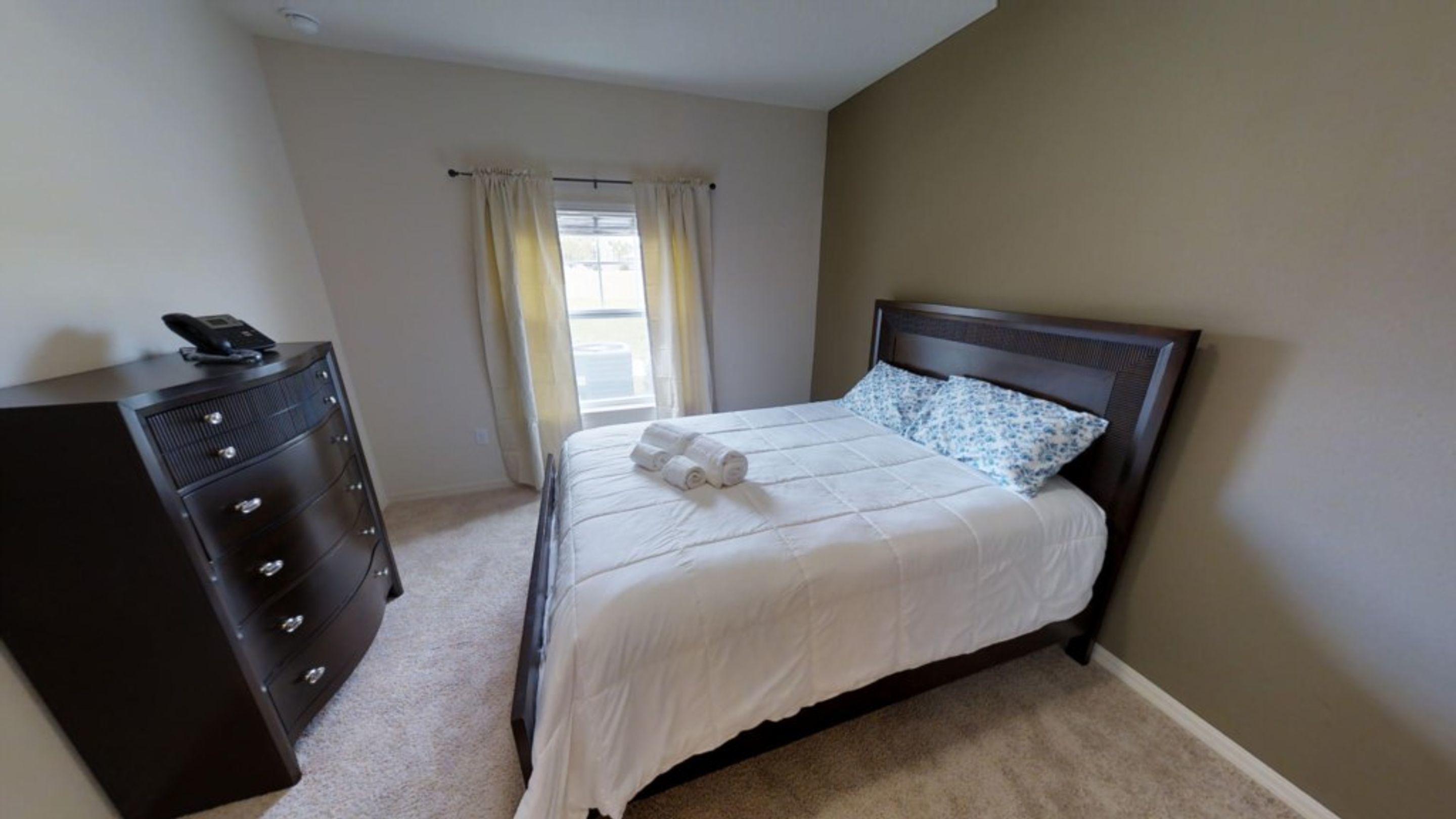 A bedroom with a bed, a dresser, and a window with curtains.