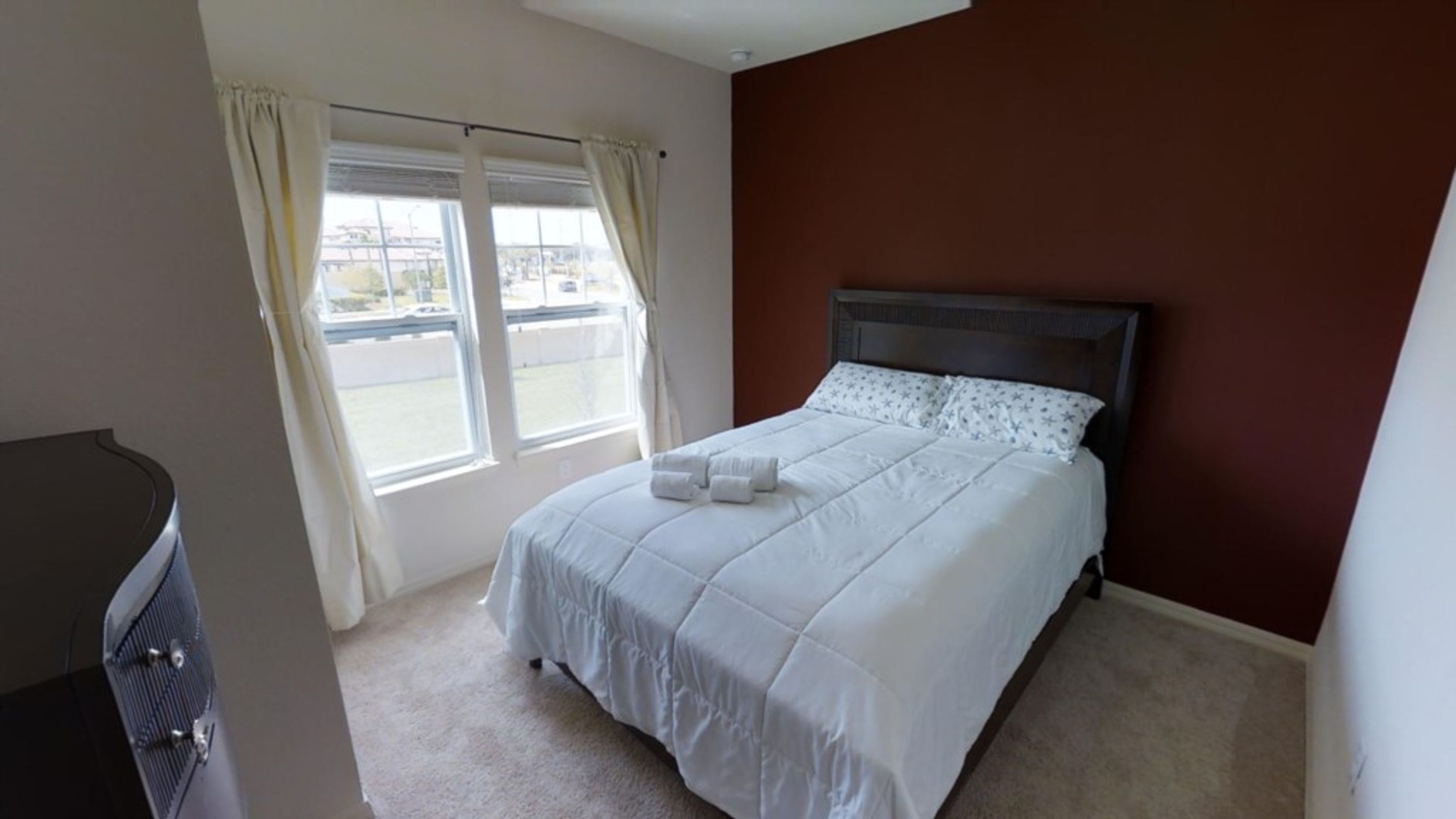 A bedroom with a bed, a window with curtains, and a view of the outside.