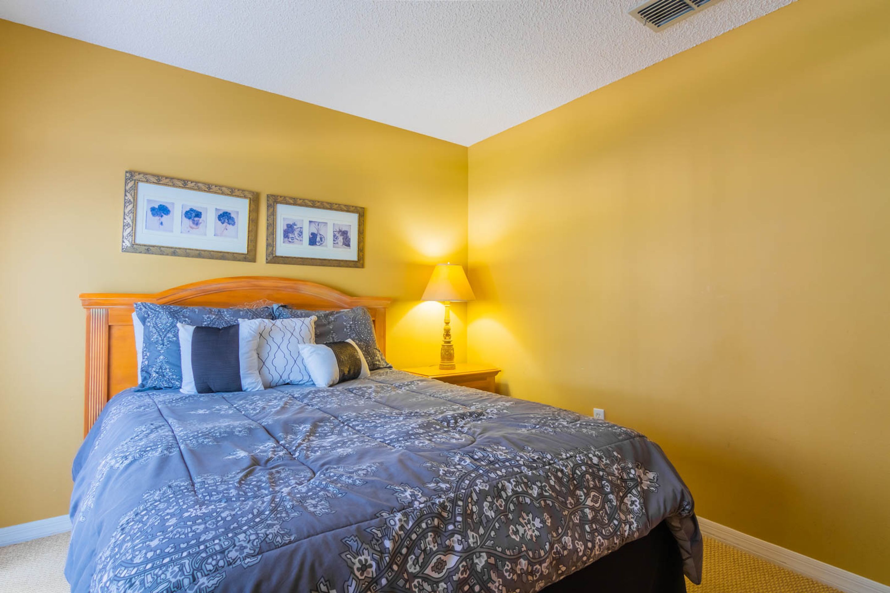 Un dormitorio con cama, lámpara de noche y dos cuadros en la pared.