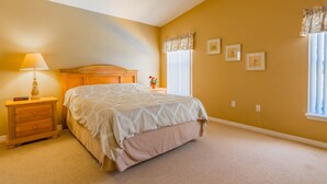 A bedroom with a bed, nightstand, lamp, window with curtains, and wall-mounted pictures.